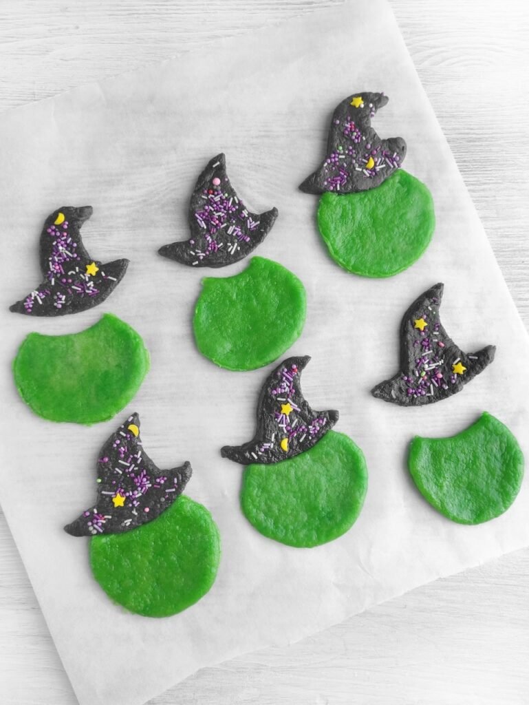 Step 3: Black cookie dough shaped into witch hats with sprinkles and green dough circles ready for assembling.
