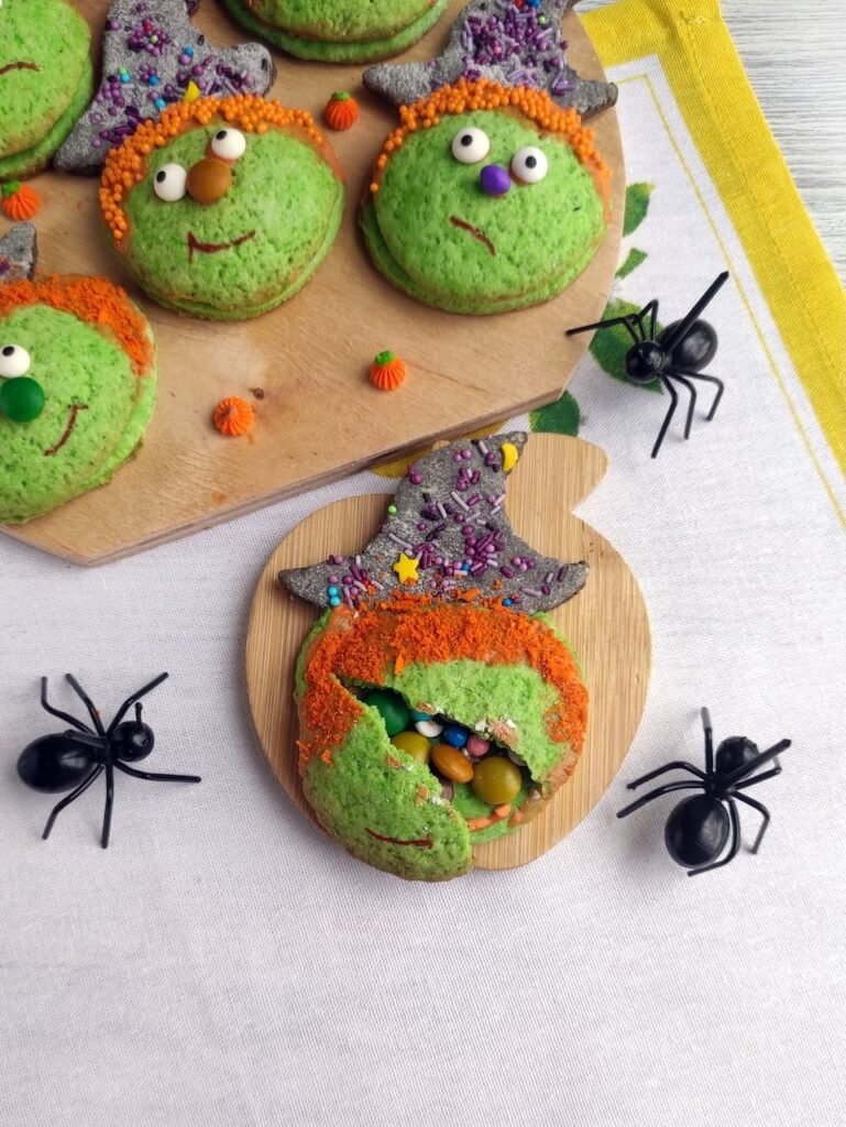 Candy-filled Halloween witch cookie broken open to reveal colorful candies inside, decorated with orange sprinkle hair, sugar eyes, and a witch hat.