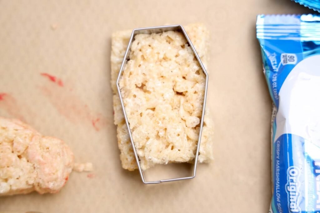 Coffin cookie cutter pressed into a Rice Krispies Treat to shape it into a spooky coffin for Halloween desserts.