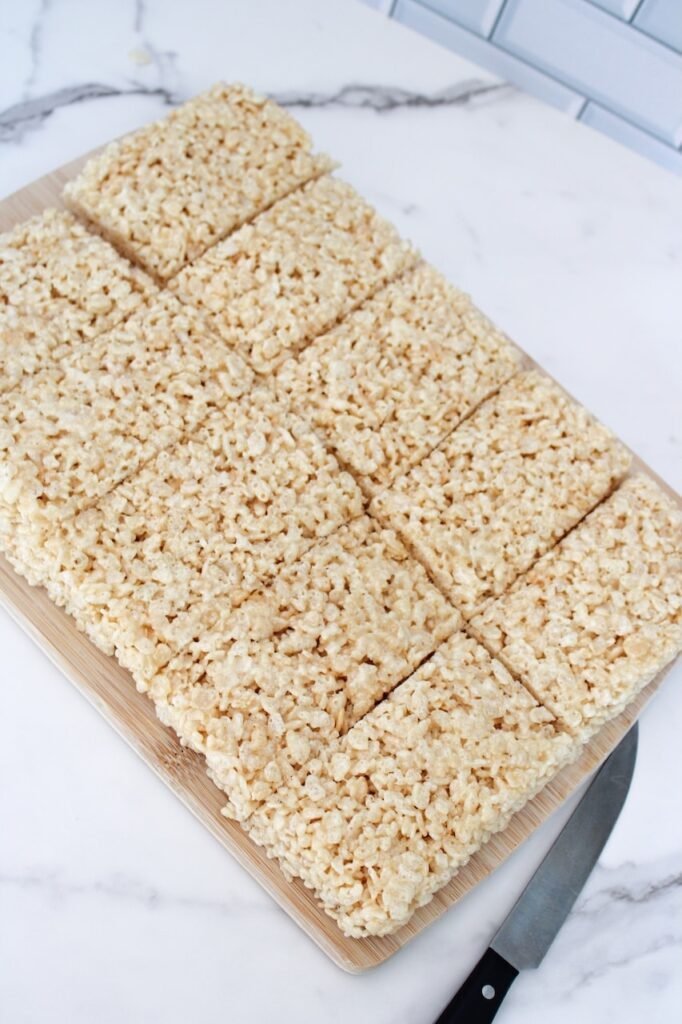Frankenstein Rice Krispies Treats cut into even rectangular bars on a wooden cutting board, ready to be decorated with green frosting, candy eyes, and chocolate hair for a fun Halloween dessert.