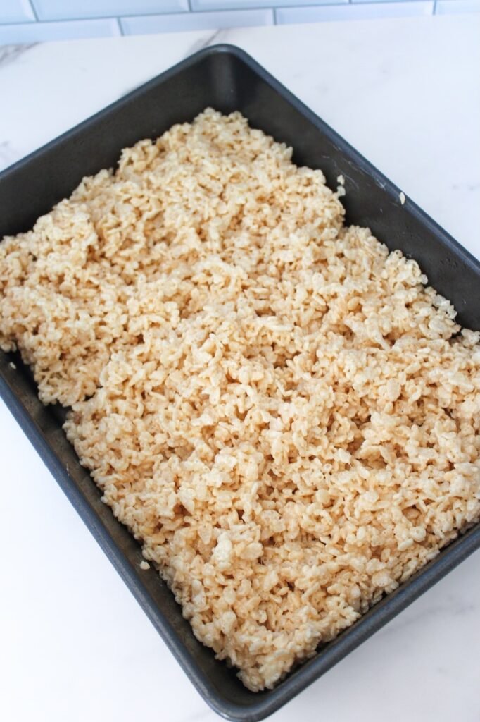 Baking pan filled with Frankenstein Rice Krispies Treats mixture of marshmallows, butter, and crispy rice cereal, pressed down evenly and ready to cool before decorating into spooky Halloween treats.