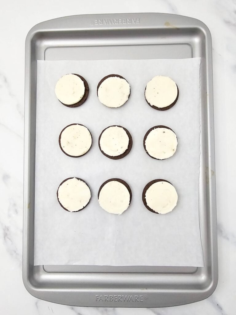 Oreo cookies with cream filling arranged on a baking sheet lined with parchment paper, step one in making no bake dessert