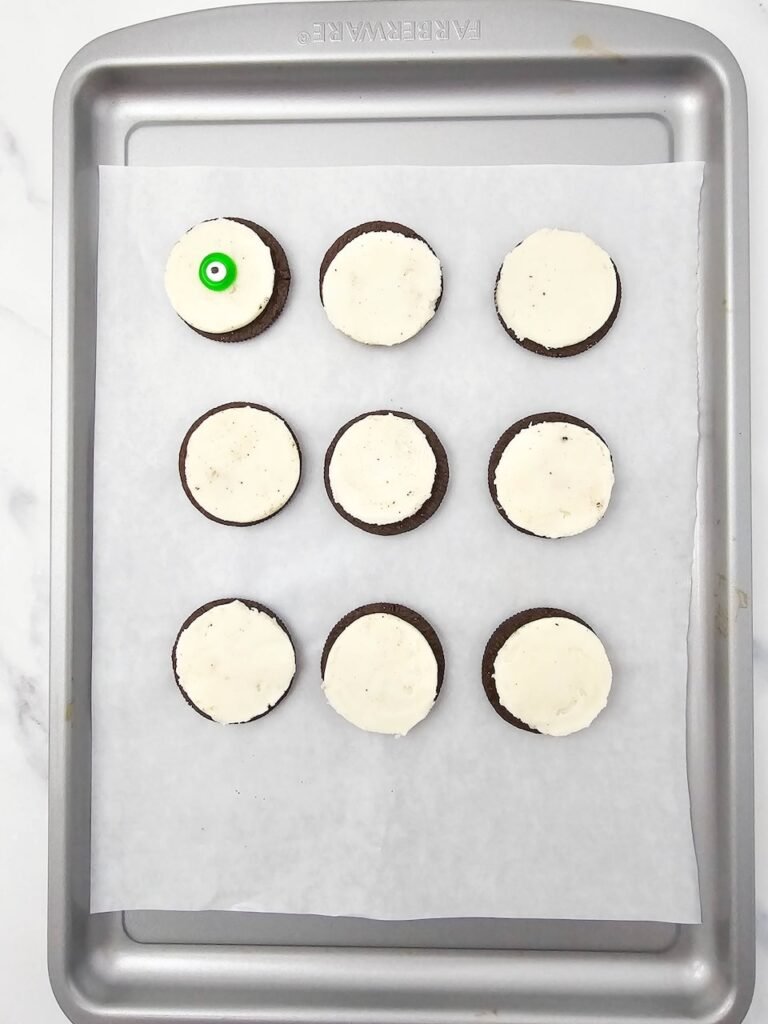 cookies on a baking sheet, one cookie decorated with a green candy eyeball to make spooky treats.