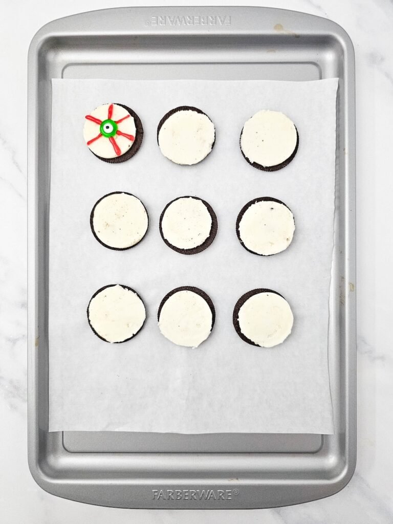 cookie on baking tray decorated with a green candy eye and red icing veins for a spooky no-bake dessert.
