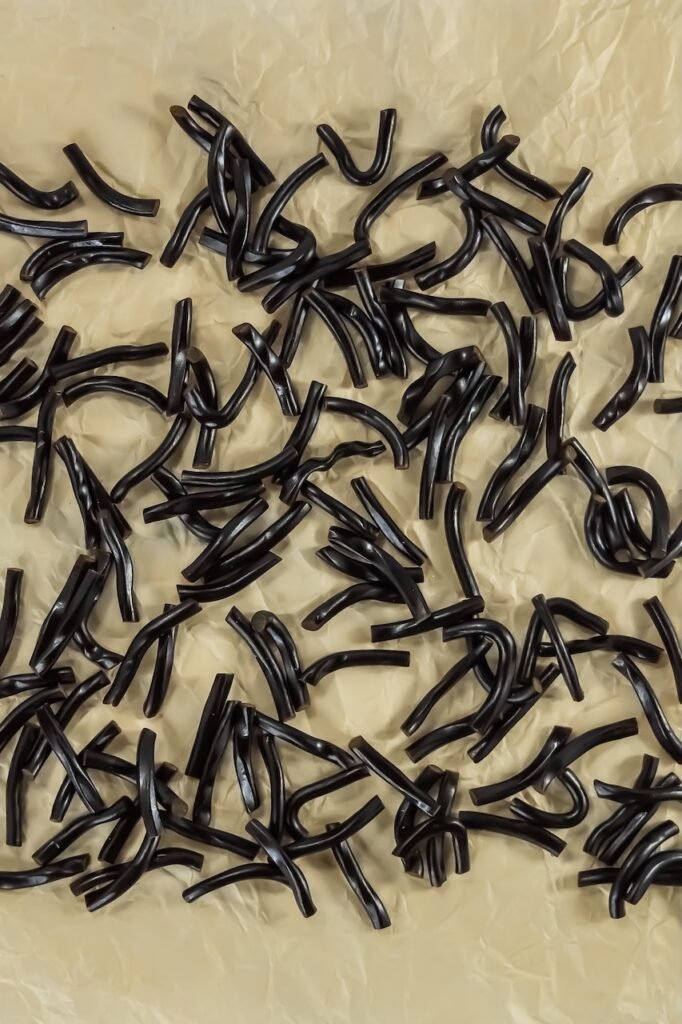 black licorice ropes cut into small 1-inch pieces and spread out on parchment paper, ready to be used as spider legs.