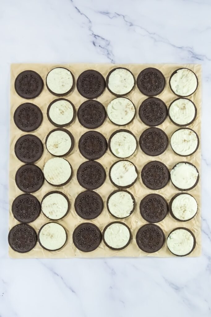 Double-Stuffed Oreos carefully twisted open and arranged on parchment paper, with cream filling on one side and cookie tops set aside.