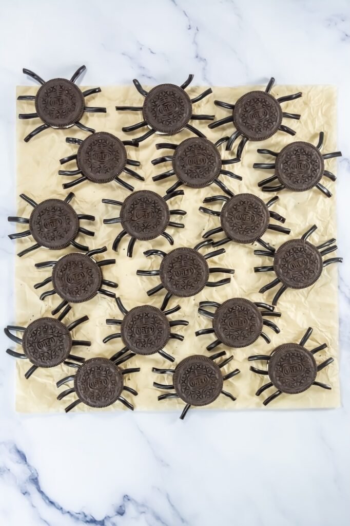 Oreo cookies with black licorice legs pressed into the cream filling, cookie tops replaced to hold the legs in place, arranged on parchment paper.