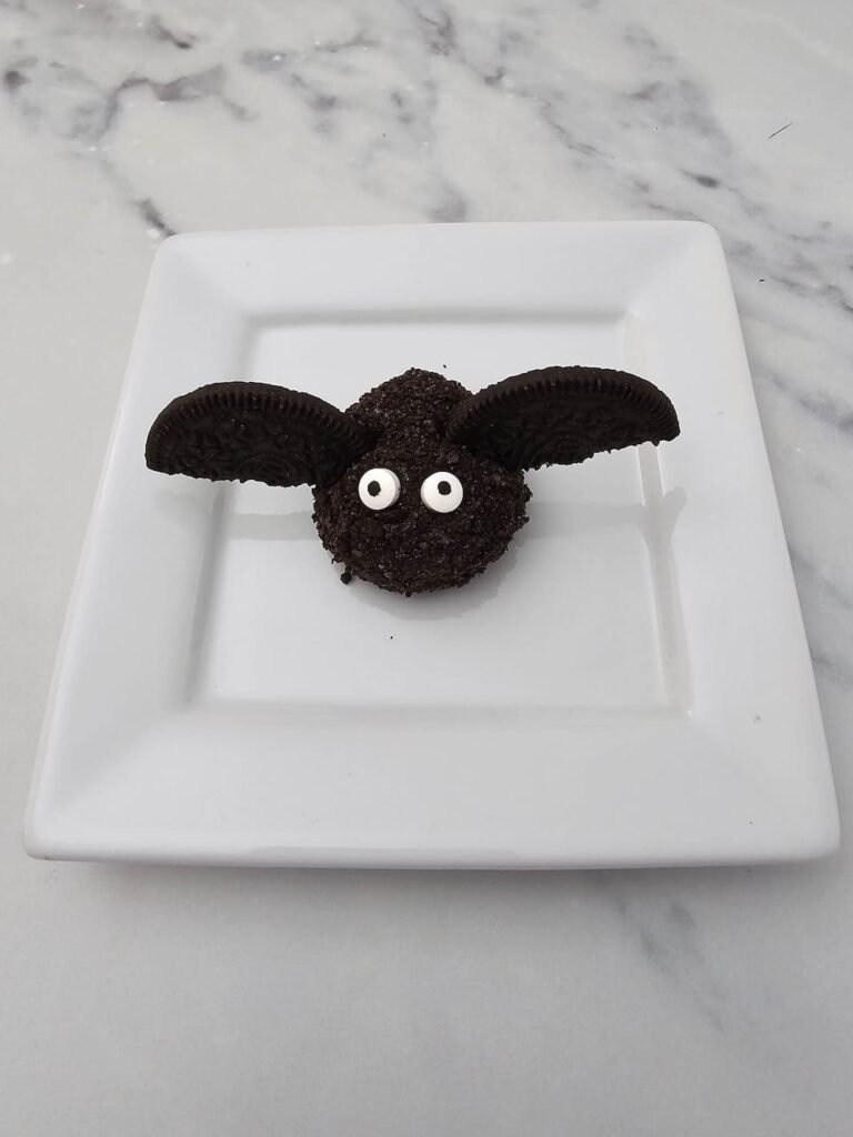Finished Oreo Truffle Bat on a white square plate, made from a coated Oreo truffle ball decorated with two Oreo cookie halves as wings and candy eyeballs for a fun no bake Halloween treat.