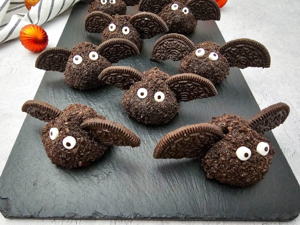 Tray of finished Oreo Truffle Bats arranged on a black slate board, each made from Oreo truffle balls coated in crumbs with Oreo cookie wings and candy eyes, a fun no bake Halloween dessert for parties.