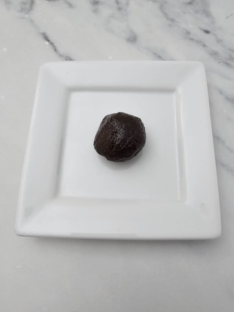 Single Oreo truffle ball rolled smooth and placed on a square white plate before being coated in crushed cookie crumbs to make Oreo Truffle Bats no bake Halloween treats.
