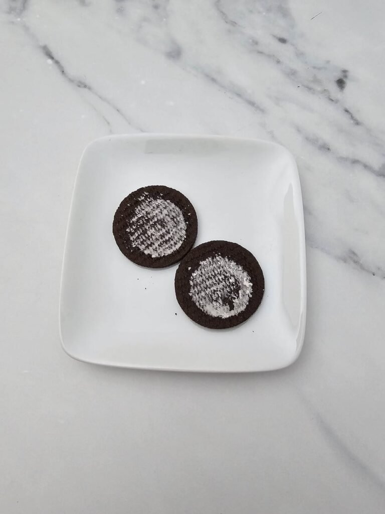 Two Oreo cookie halves with the cream filling removed on a white plate, prepared to be used as bat wings for this Halloween treats.