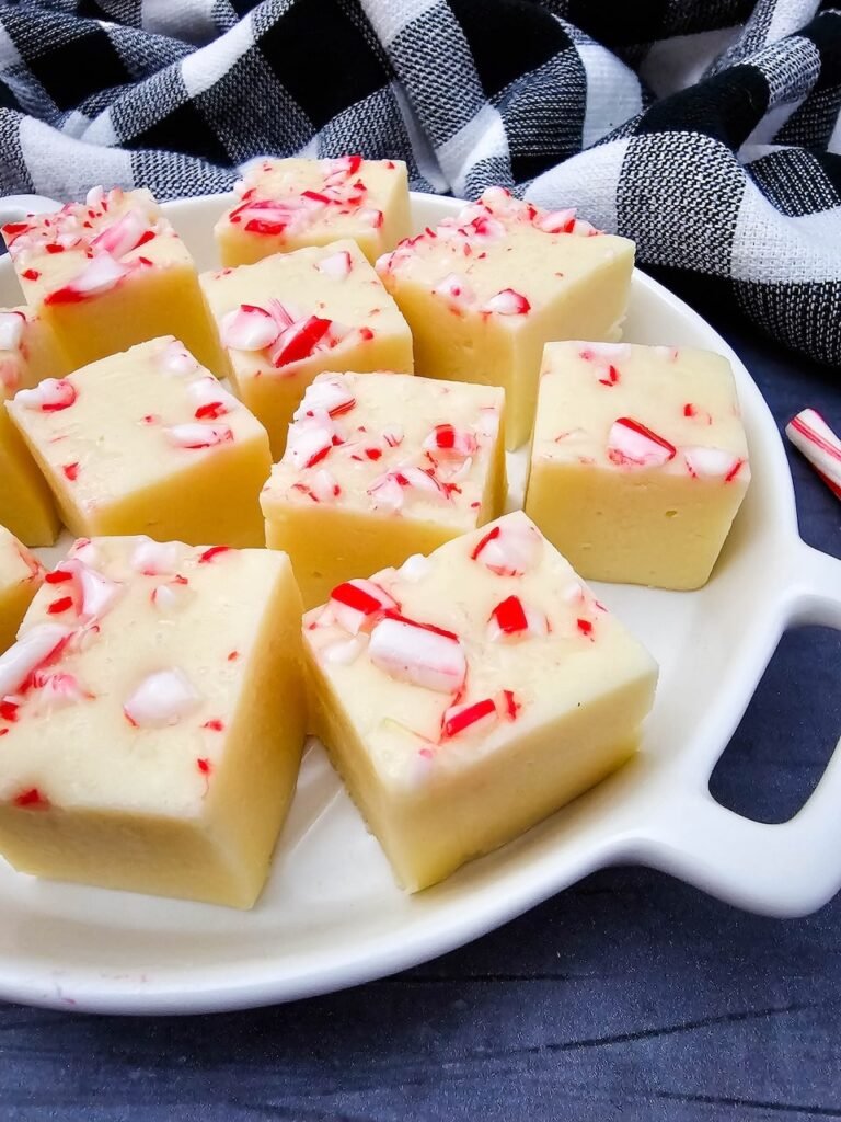 Plated squares of candy cane fudge with crushed peppermint on top, styled with candy canes and buffalo plaid.