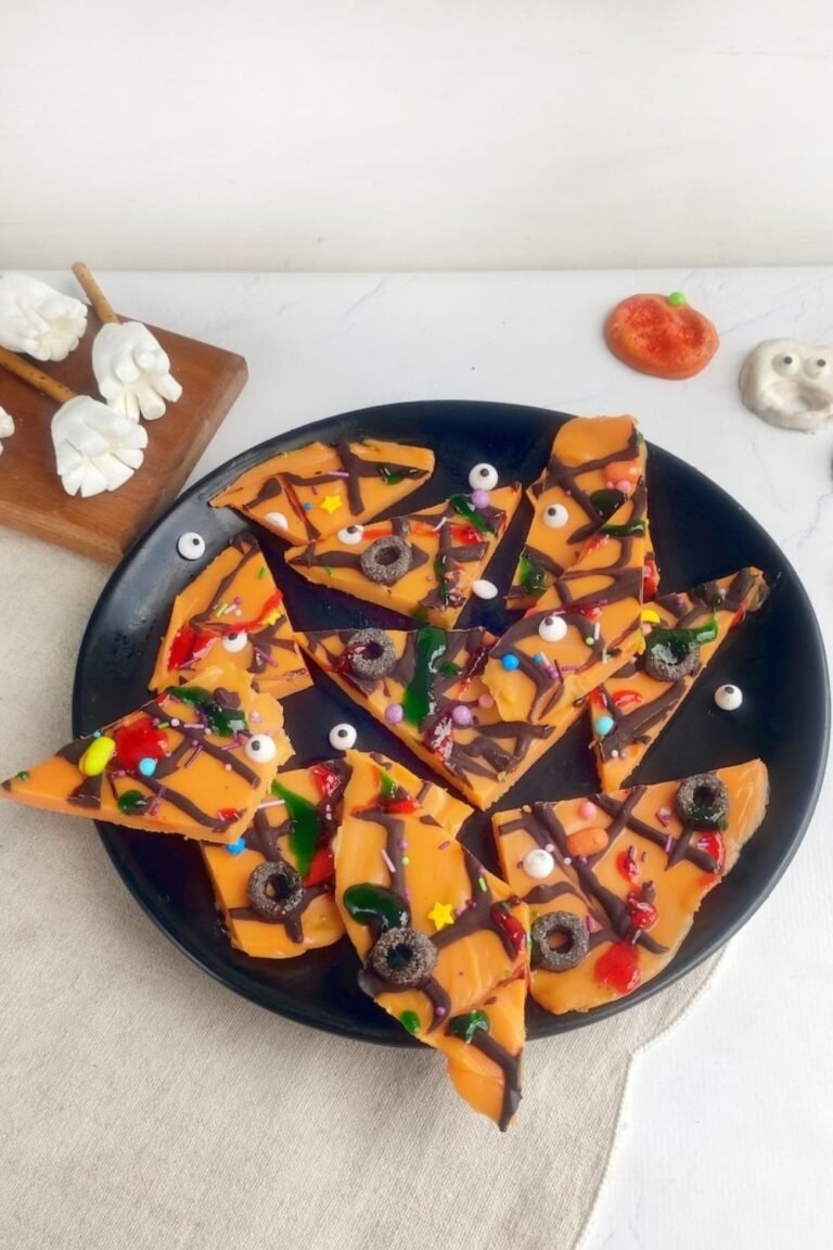 Halloween candy bark shards decorated with spooky toppings, served on a black plate as a fun party snack or leftover candy recipe idea.