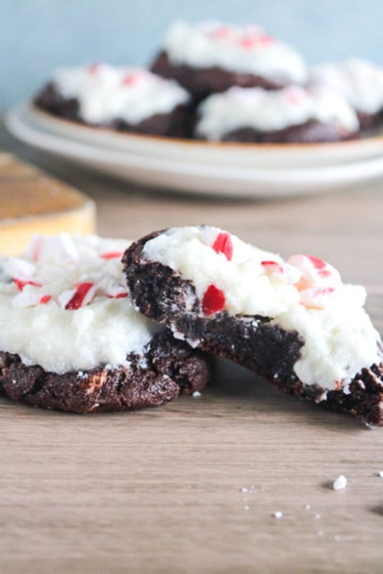 Soft chocolate peppermint bark cookies topped with creamy white frosting and crushed peppermint candies on a wooden table.