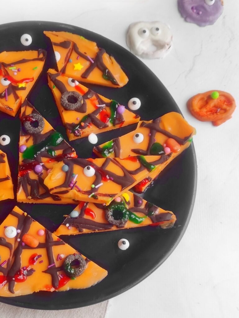No-bake Halloween dessert featuring broken pieces of candy bark topped with spooky sugar eyeballs, sprinkles, Tic-Tacs, and chocolate rings styled with festive candy props.