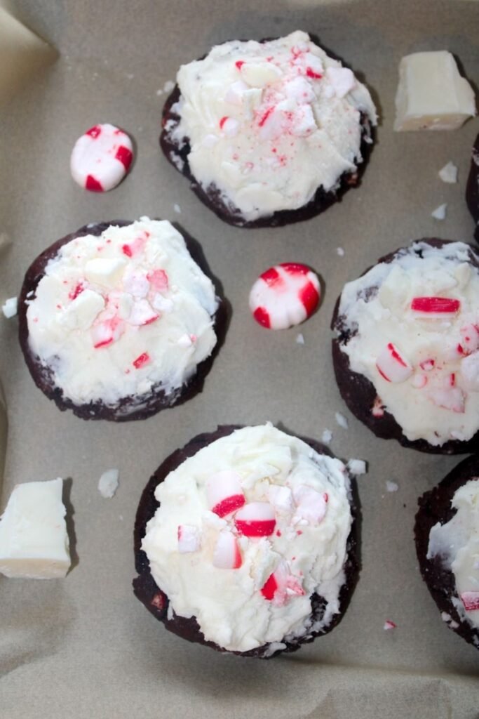 Freshly frosted topped with crushed peppermint candies and white chocolate pieces on parchment paper.