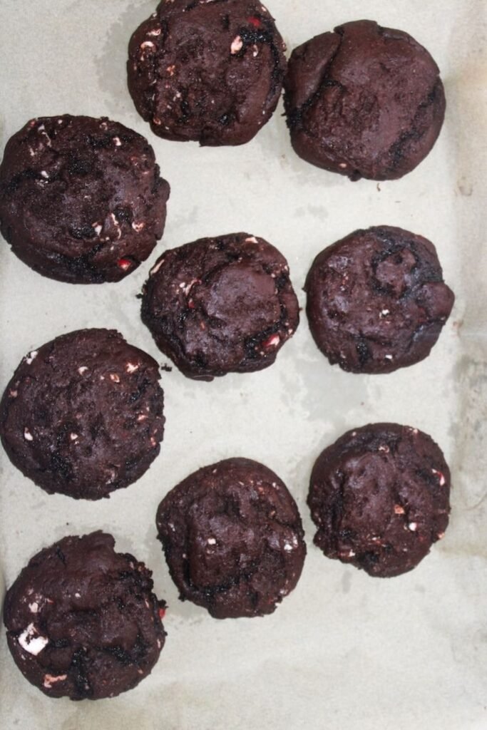 A tray of freshly baked peppermint bark cookies with melted chocolate and peppermint pieces on parchment paper.