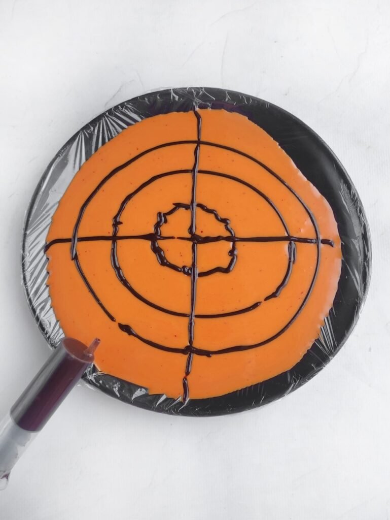 step three of Halloween candy bark recipe showing dark chocolate circles piped on top of orange base before creating spiderweb design.
