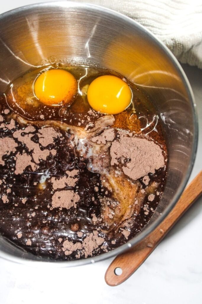 A metal mixing bowl filled with chocolate cake mix, eggs, and melted butter being combined to make peppermint bark cookie dough.