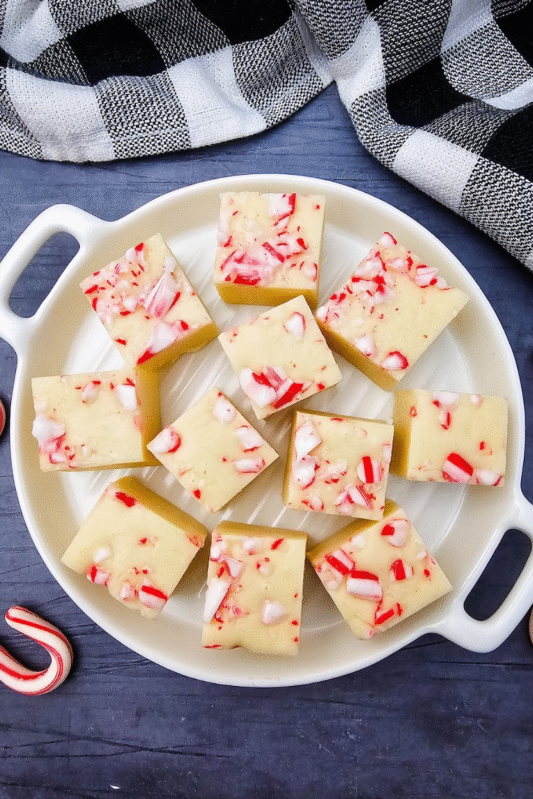 Flat lay of white chocolate peppermint fudge squares on a white plate with candy canes and a plaid napkin.