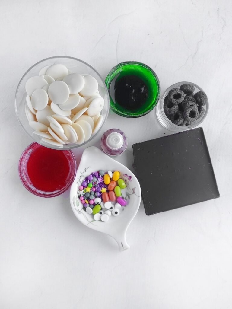 Overhead view of no-bake Halloween candy bark ingredients such as chocolate, jams, sugar eyeballs, sprinkles, and gel food coloring ready to be used.
