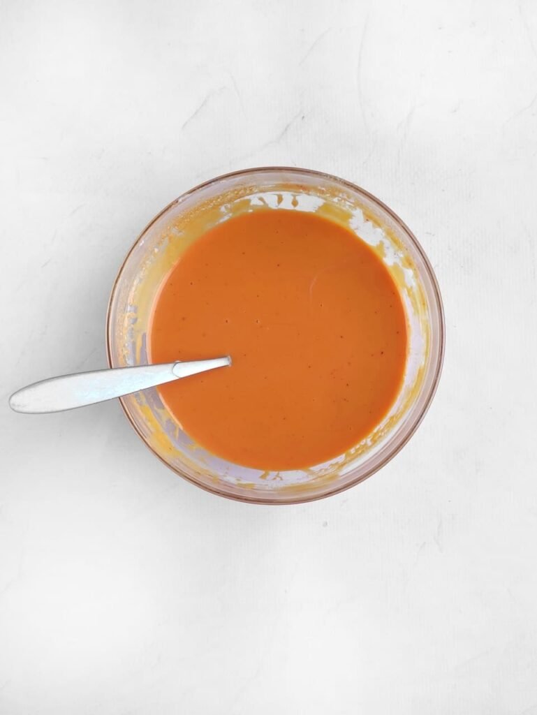 Bowl of melted white chocolate tinted with orange gel food coloring, ready to be used as the base for Halloween candy bark recipe.