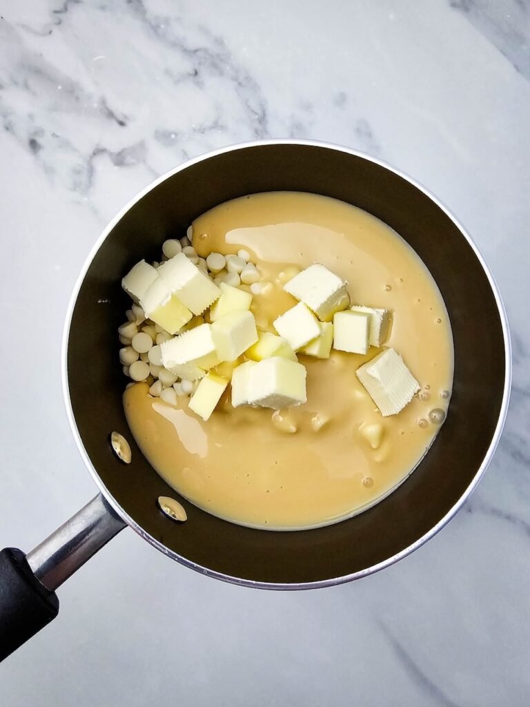 Butter cubes, white chocolate chips, and sweetened condensed milk in a saucepan before melting for candy cane fudge.