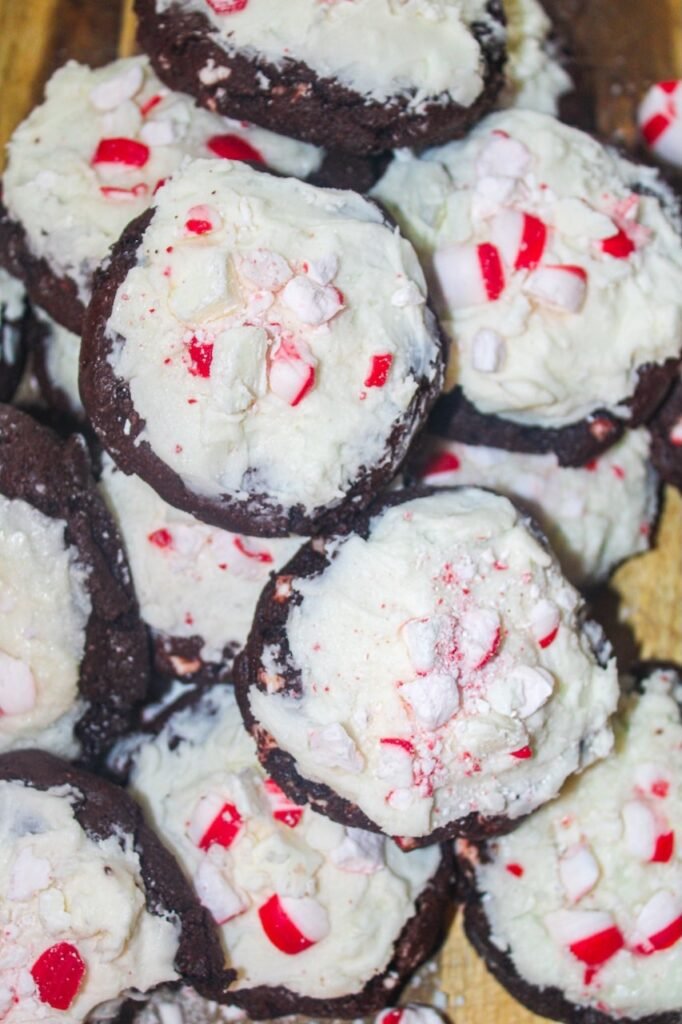A close-up of a stack of peppermint bark cookies topped with creamy white chocolate frosting and crushed peppermint candies.