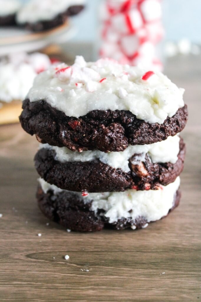 A stack of thick, chewy peppermint bark cookies layered with creamy white chocolate frosting and topped with crushed peppermint candy.