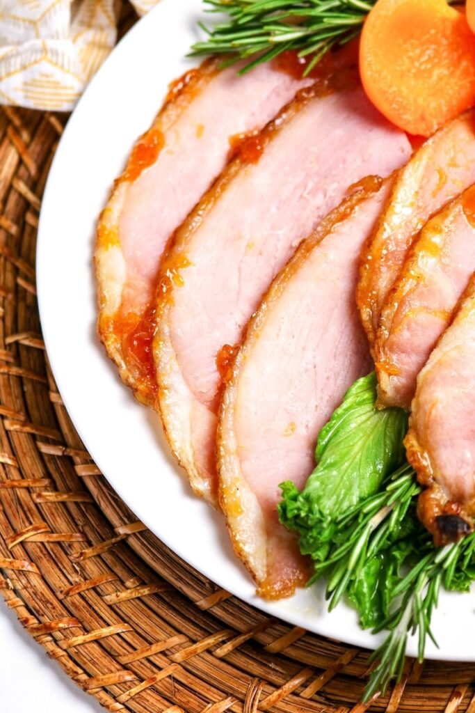 close-up of sliced apricot glazed ham with shiny caramelized glaze, garnished with rosemary and apricot halves — an easy holiday baked ham recipe perfect for Easter or Christmas