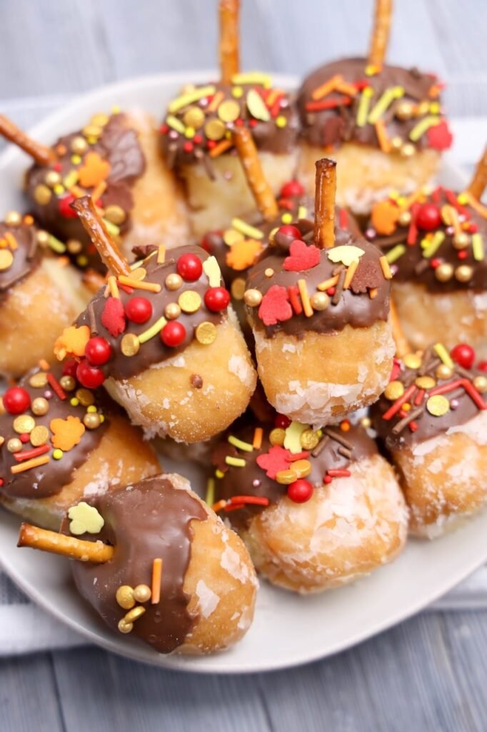Close-up of chocolate-dipped acorn donut holes decorated with colorful fall sprinkles and pretzel stems.