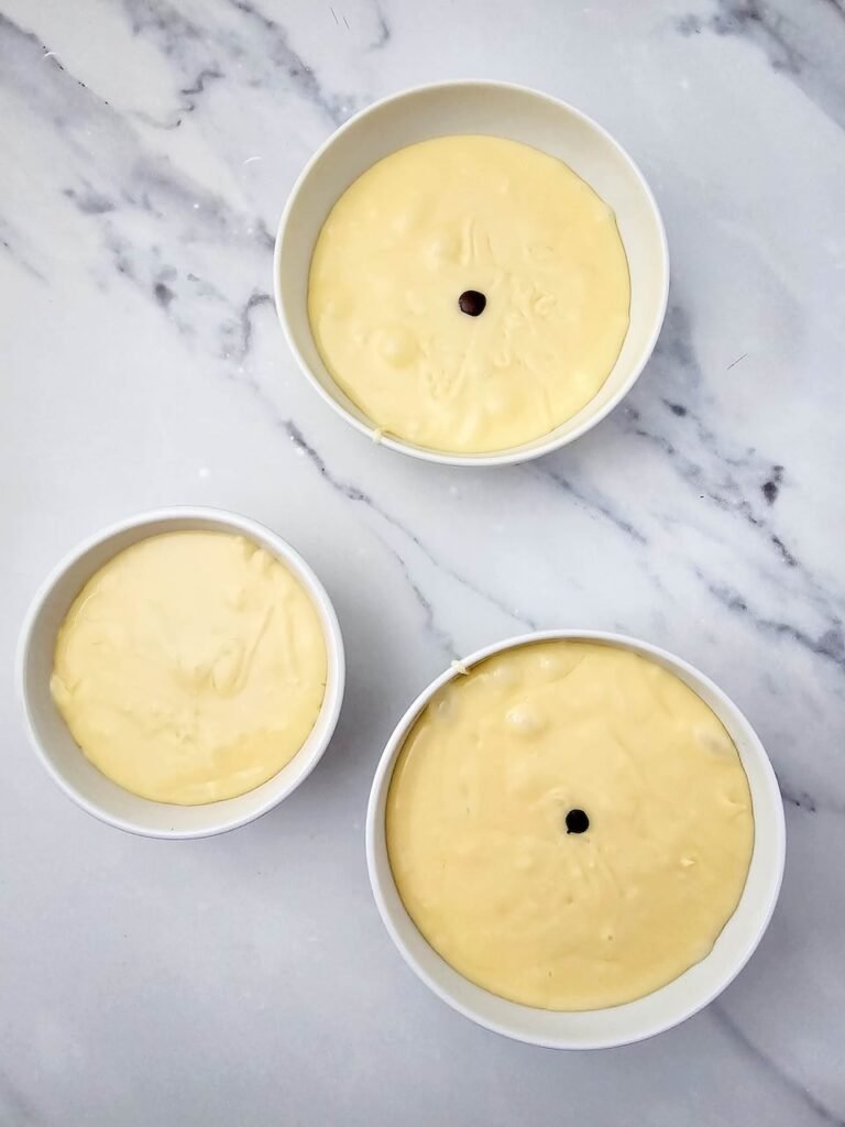 Divided bowls of melted white chocolate fudge with red and green food coloring drops ready to stir for swirls.