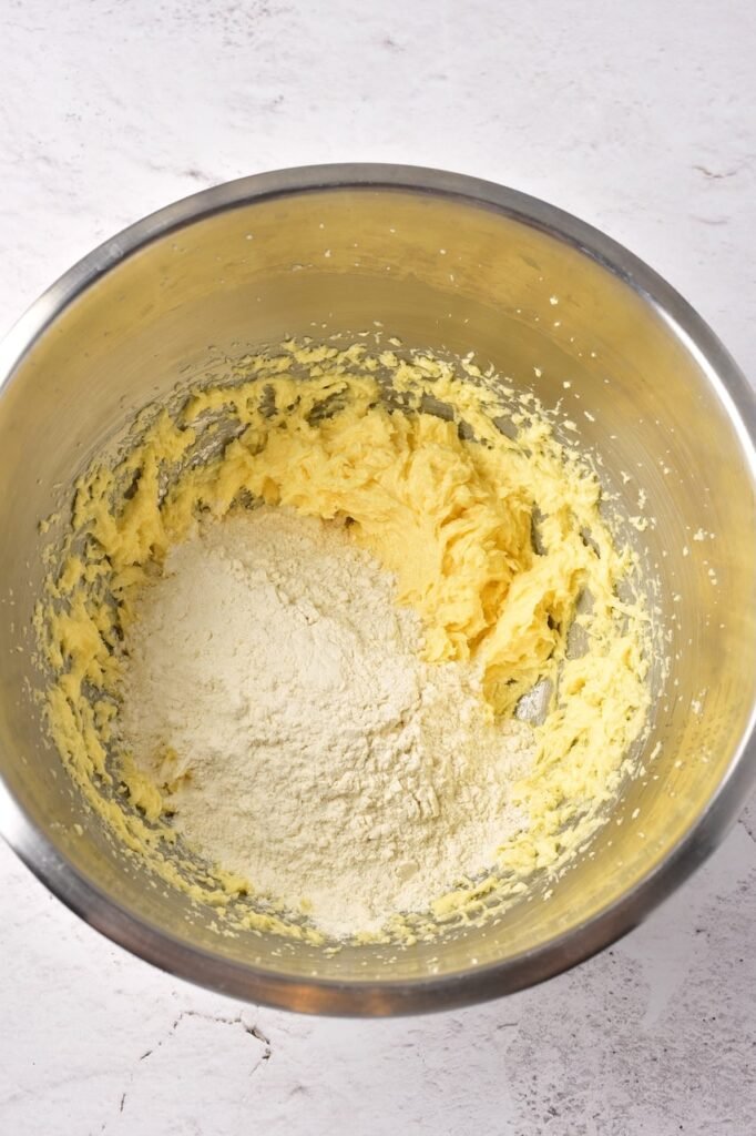 adding flour mixture to creamed butter, sugar, and egg in a mixing bowl to make Christmas sugar cookie dough.