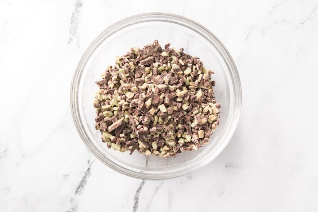 Glass bowl filled with Andes Creme de Menthe baking chips on a white marble surface, showing the mint chocolate pieces before melting.