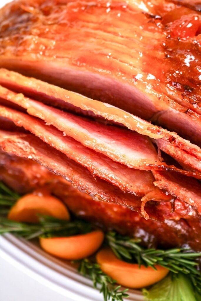 Close-up of spiral-cut apricot glazed ham with shiny caramelized glaze, sliced and ready to serve with apricots and rosemary — a juicy baked holiday ham for Easter or Christmas dinner.