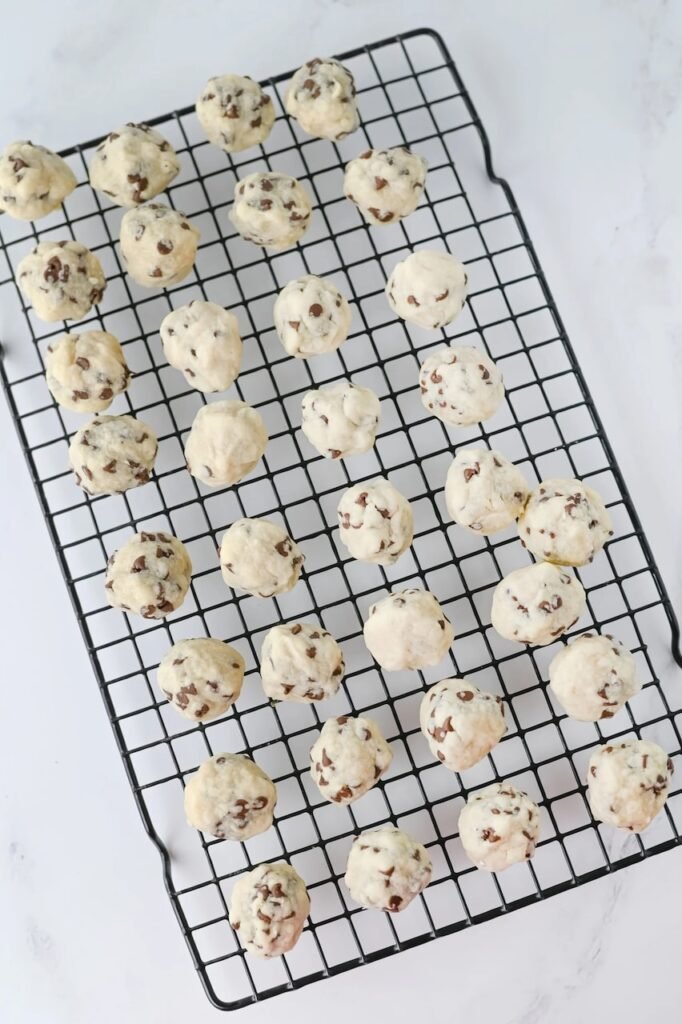 Freshly baked chocolate chip snowball cookies cooling on a wire rack before being rolled in powdered sugar.