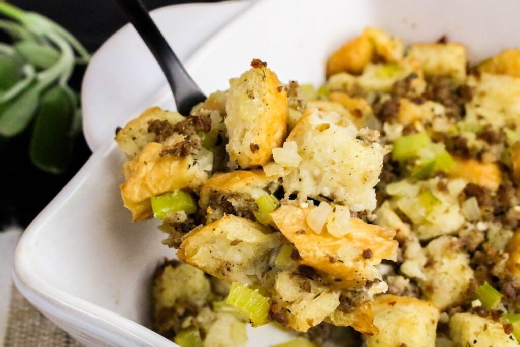 Golden baked sage and sausage herb stuffing served in a white casserole dish with crispy bread cubes, sausage, and celery.