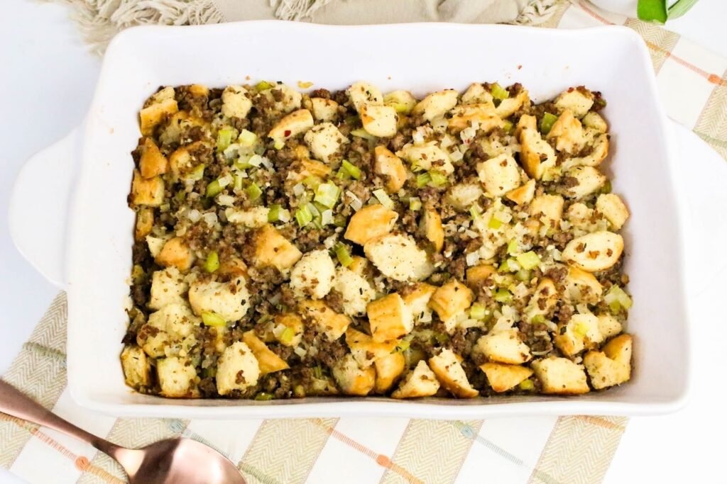 Golden baked sage and sausage herb stuffing in a white casserole dish topped with crisp bread cubes and celery.