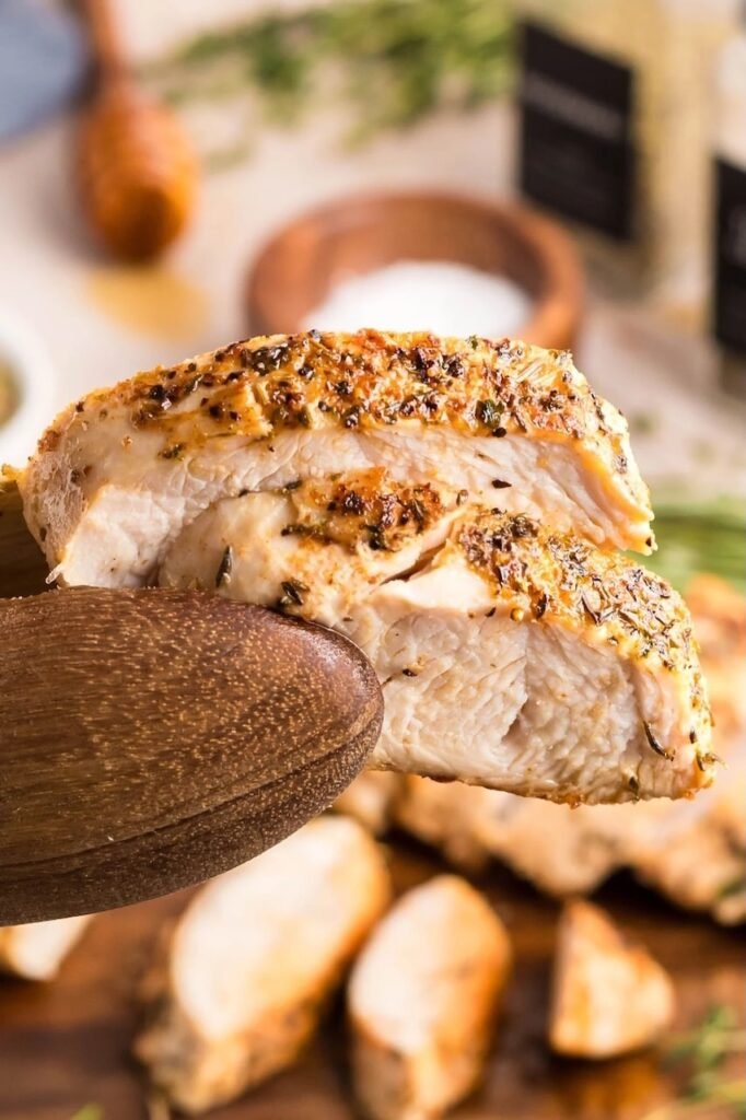 Close-up of juicy, golden oven roasted turkey tenderloin held on a wooden spoon, showing tender texture and herb crust.