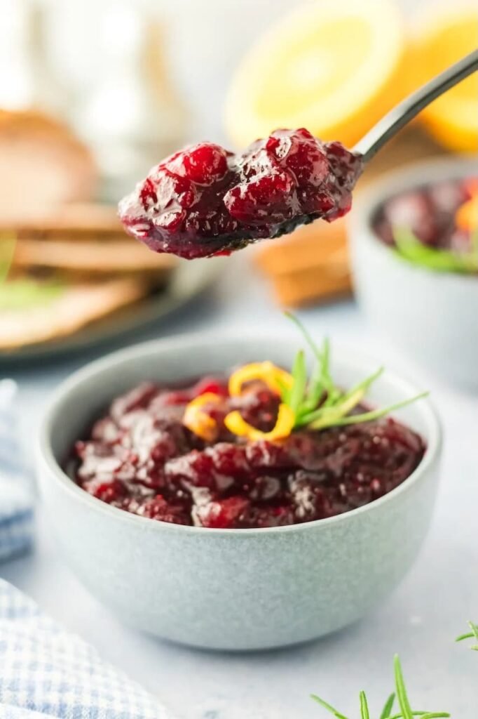 Spoonful of homemade cranberry sauce with orange zest held over a bowl, showing its thick, glossy texture.