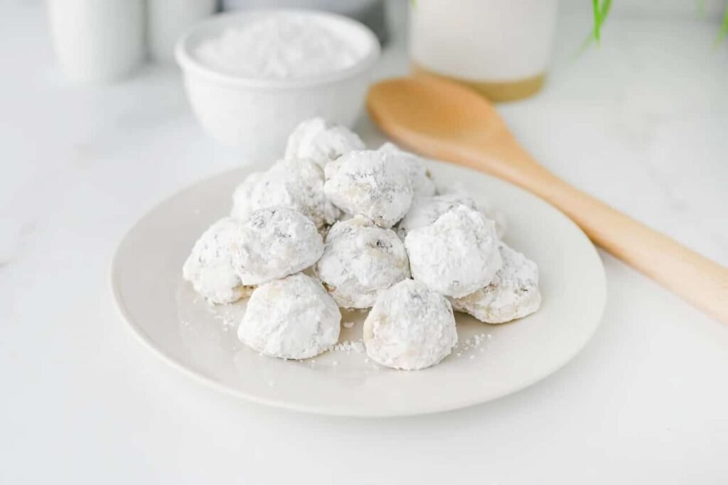 Buttery chocolate chip snowball cookies covered in powdered sugar stacked on a white plate.