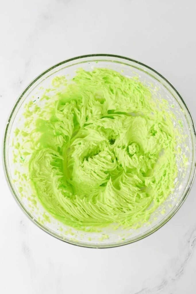 Bright neon-green buttercream frosting whipped in a glass bowl, showing a fluffy and creamy texture.