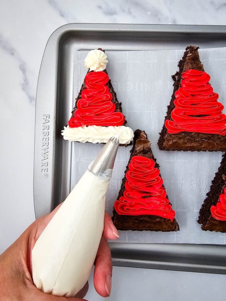 Adding white frosting trim to red iced brownie triangles to finish.