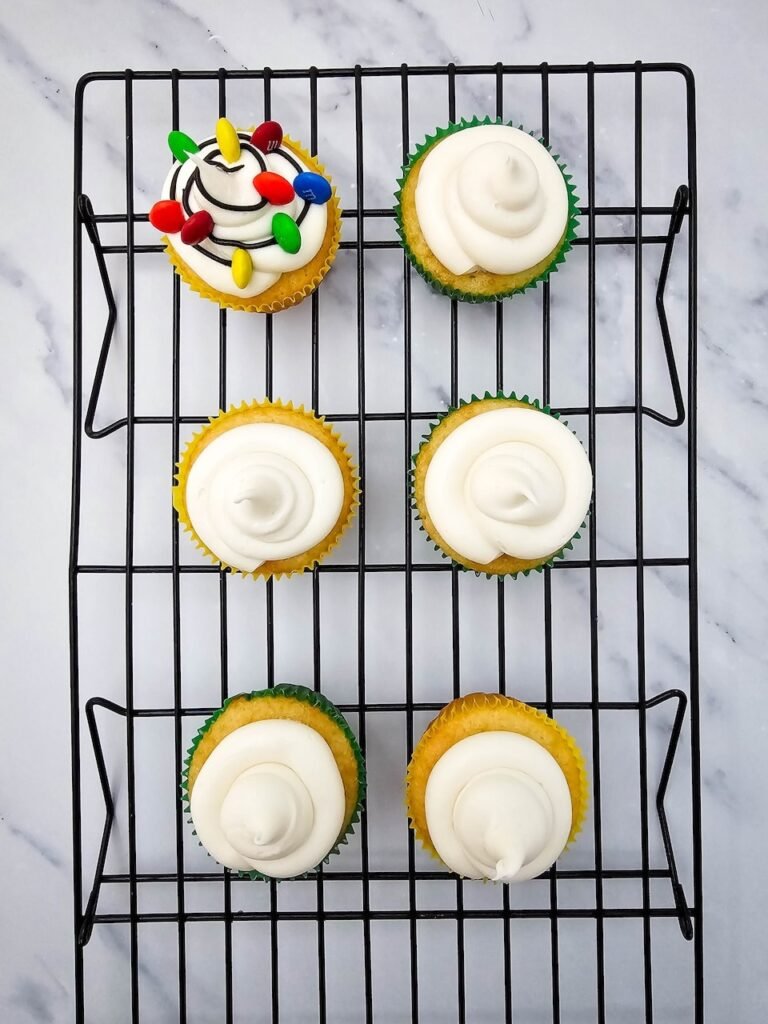 Decorating by pressing colorful M&Ms onto black icing lines to create festive candy light bulbs.