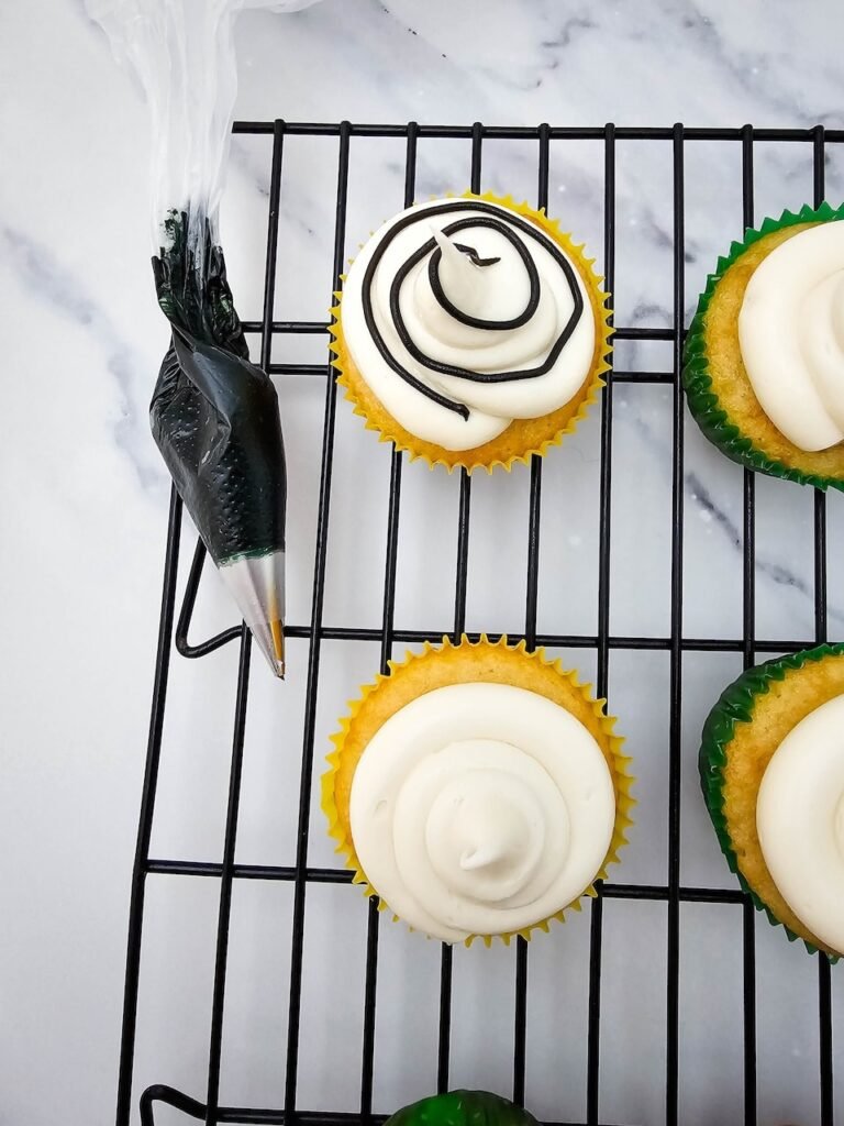 Piping black icing onto frosted cupcakes to create the light string design.