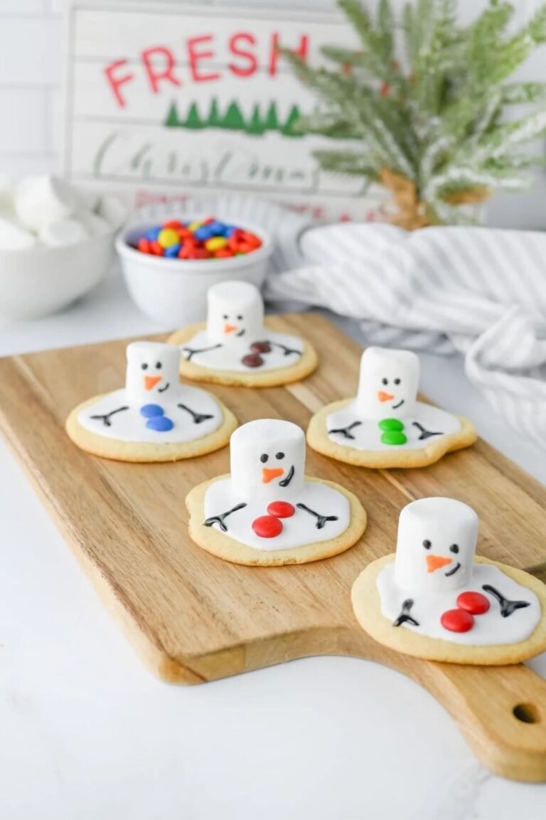 Finished melted snowman cookies decorated with marshmallow heads, icing faces, and colorful candy buttons on a wooden board with festive holiday decor.