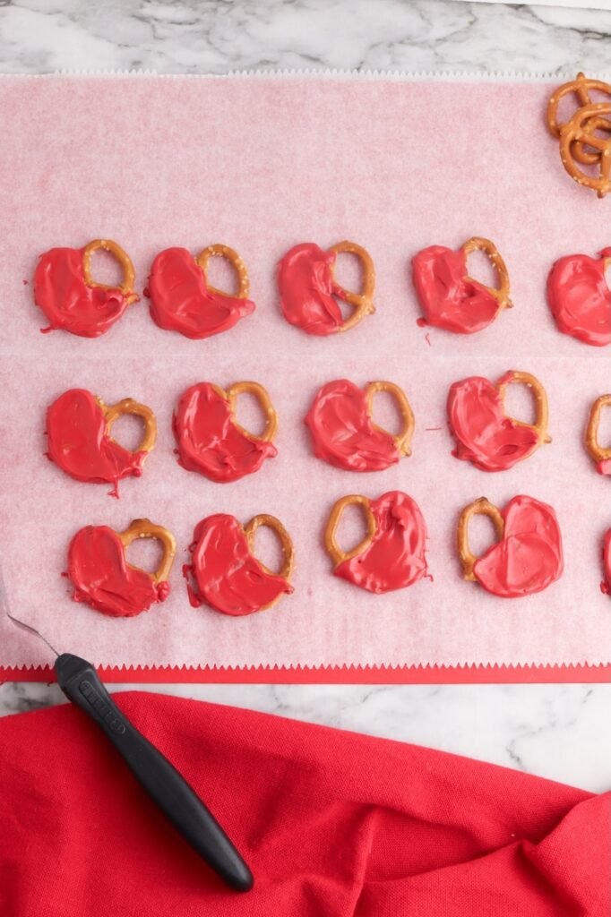 Mini pretzels half-dipped in red melted candy laid on parchment paper to harden.
