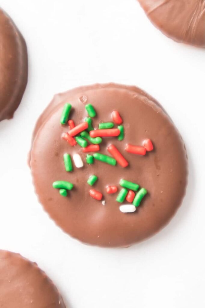 Close-up of a single Christmas Thin Mint Cookie covered in smooth mint chocolate and topped with red, green, and white sprinkles, showing detail of this easy no-bake holiday cookie made with Ritz crackers.