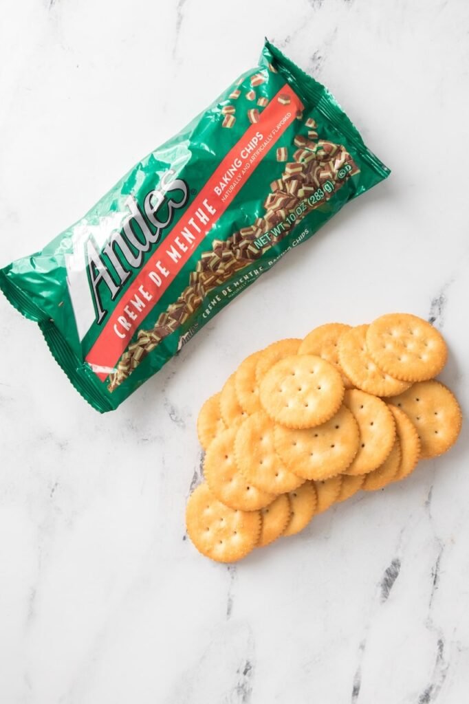 Andes Creme de Menthe baking chips and Ritz crackers arranged on a white marble surface, showing the simple two-ingredient setup for making easy no-bake with a mint chocolate coating.