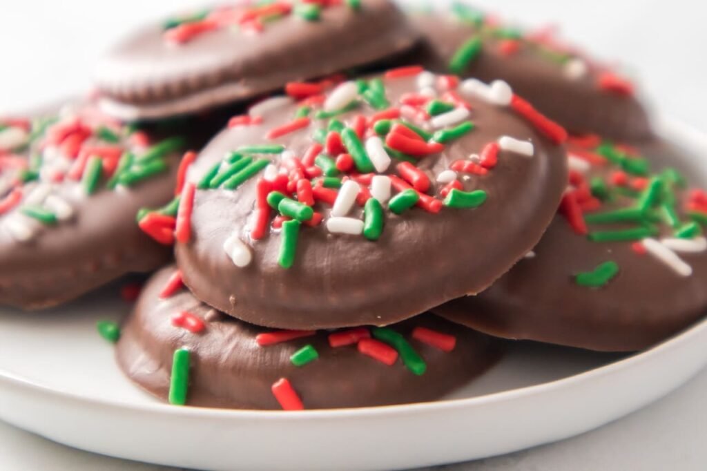 Close-up of chocolate-covered Christmas Thin Mint Cookies topped with red, green, and white sprinkles on a white plate, showing the festive no-bake holiday treat made with Ritz crackers and Andes mint chocolate.